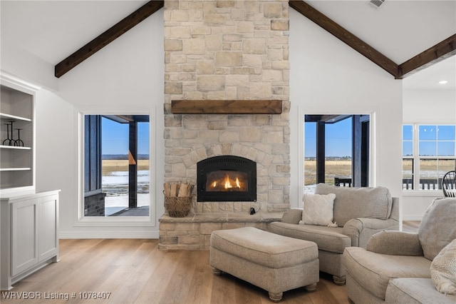 living room with a water view, light wood-type flooring, a fireplace, high vaulted ceiling, and beam ceiling