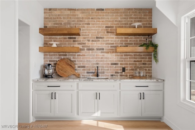 bar featuring light stone countertops, white cabinetry, and sink