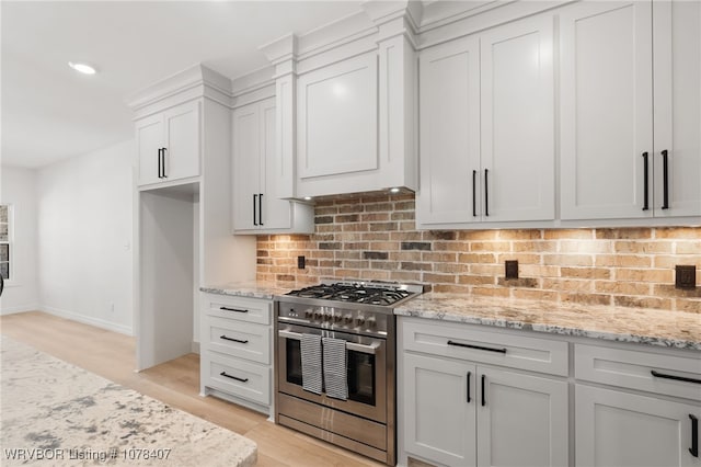 kitchen featuring decorative backsplash, white cabinetry, light wood-type flooring, light stone countertops, and high end stainless steel range