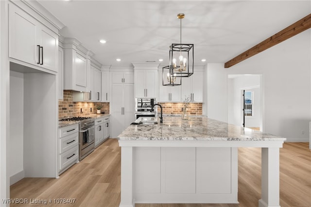 kitchen featuring light stone countertops, decorative light fixtures, an island with sink, sink, and stainless steel stove