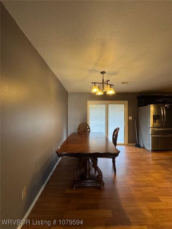 unfurnished dining area featuring baseboards, a textured ceiling, a chandelier, and light wood finished floors