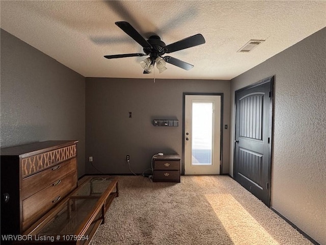 interior space featuring visible vents, carpet floors, a ceiling fan, and a textured wall