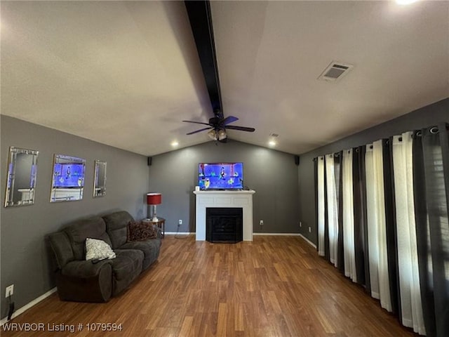 living room with wood finished floors, visible vents, vaulted ceiling with beams, a fireplace, and ceiling fan