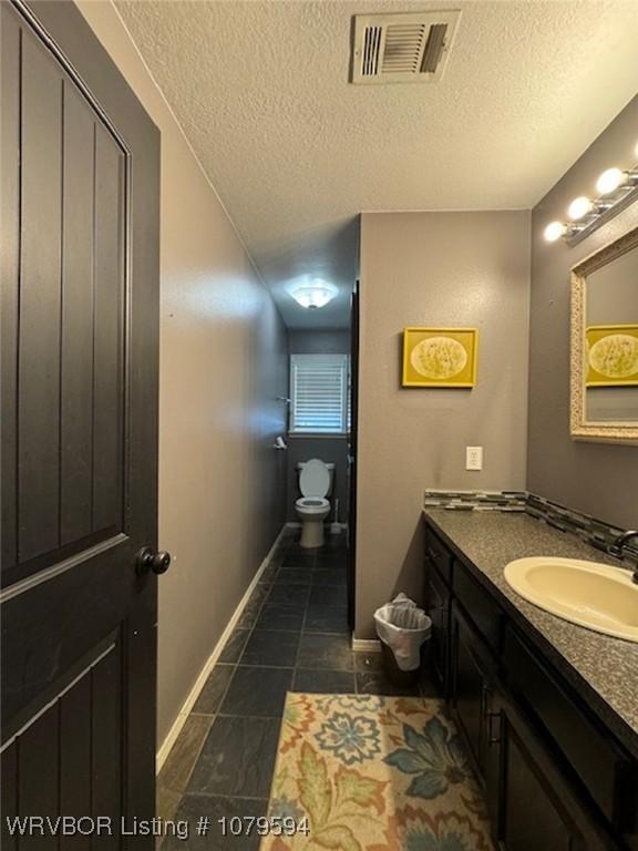 bathroom featuring visible vents, baseboards, toilet, vanity, and a textured ceiling