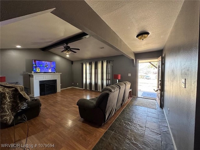 living room with stone tile floors, a ceiling fan, baseboards, lofted ceiling with beams, and a textured ceiling