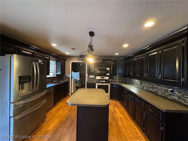 kitchen with stainless steel appliances, a kitchen island, dark cabinetry, and light wood-style flooring