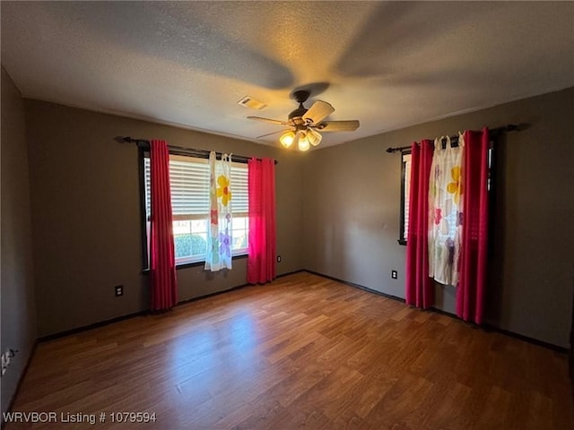 empty room featuring ceiling fan, visible vents, a textured ceiling, and wood finished floors