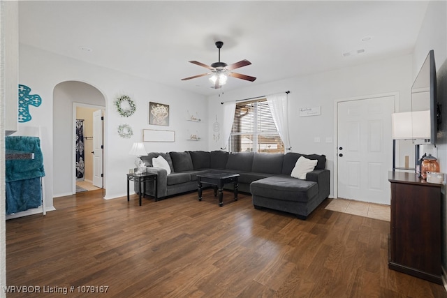 living room with dark wood-style floors, ceiling fan, and arched walkways