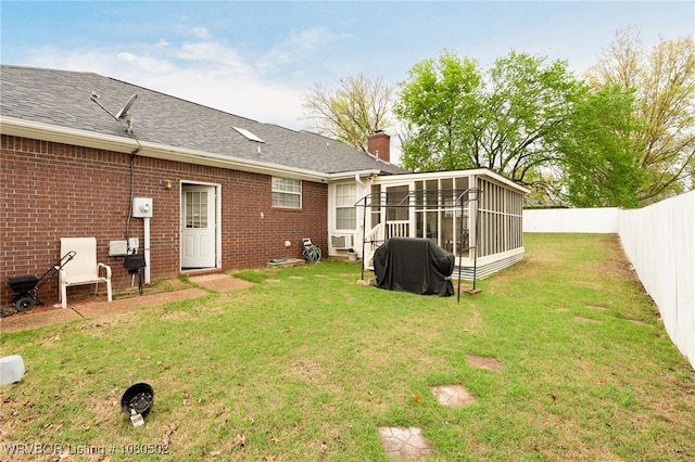 rear view of property featuring a sunroom, brick siding, a fenced backyard, a lawn, and a chimney