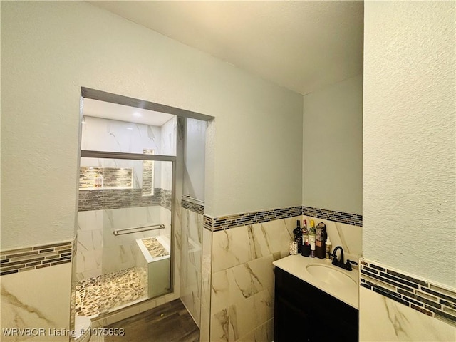 bathroom featuring a tile shower, vanity, and tile walls