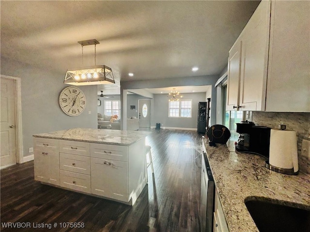 kitchen featuring light stone countertops, pendant lighting, ceiling fan with notable chandelier, and white cabinetry