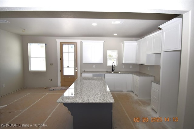 kitchen with light stone counters, visible vents, white cabinetry, a kitchen island, and a sink