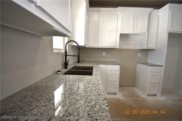 kitchen featuring light stone counters, white cabinets, and a sink