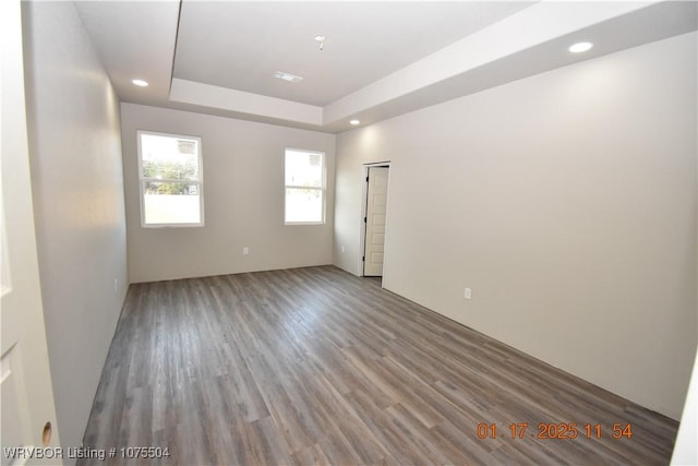 empty room featuring a raised ceiling, wood finished floors, and recessed lighting