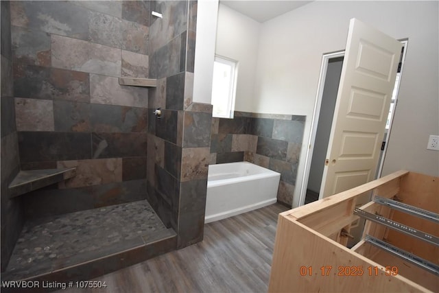 bathroom featuring tiled shower, wood finished floors, a bath, and tile walls