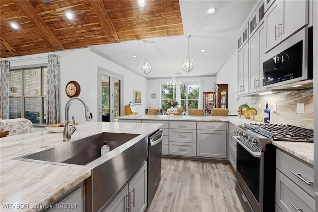 kitchen featuring gray cabinets, backsplash, appliances with stainless steel finishes, a peninsula, and light stone countertops