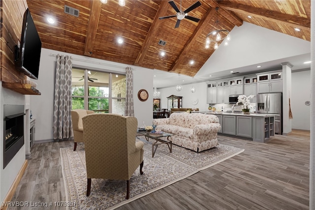 living room with beamed ceiling, light wood-style flooring, wooden ceiling, a glass covered fireplace, and high vaulted ceiling