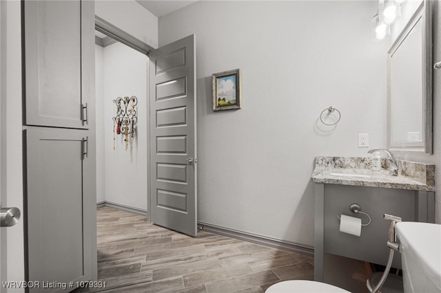 bathroom with vanity, toilet, wood finished floors, and baseboards