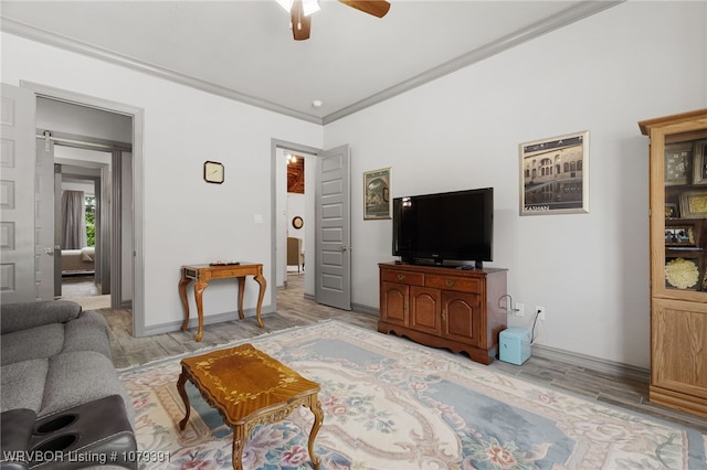 living area with baseboards, light wood-type flooring, a barn door, ornamental molding, and a ceiling fan