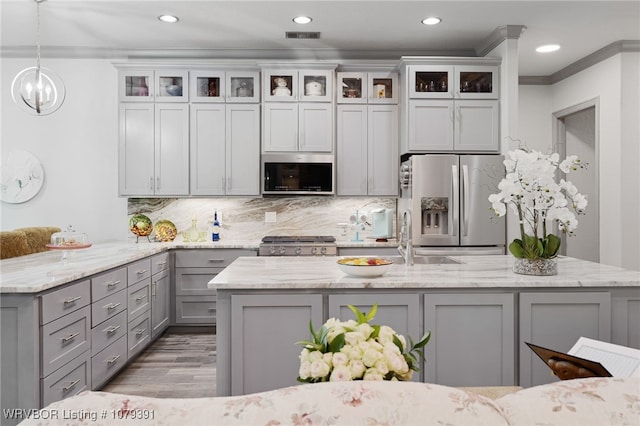 kitchen featuring ornamental molding, gray cabinets, a sink, light stone counters, and appliances with stainless steel finishes