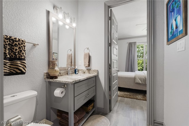 bathroom with toilet, ornamental molding, wood finished floors, connected bathroom, and vanity