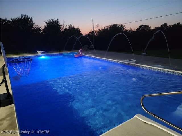 pool at dusk featuring an outdoor pool and a diving board