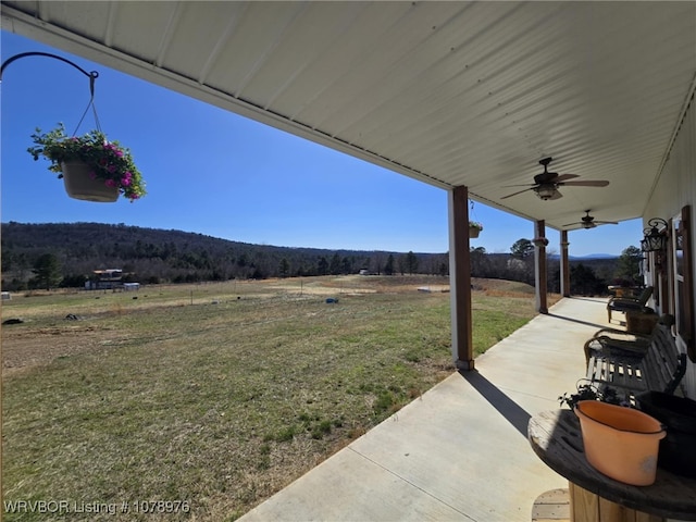 view of yard with a patio, a ceiling fan, and a view of trees