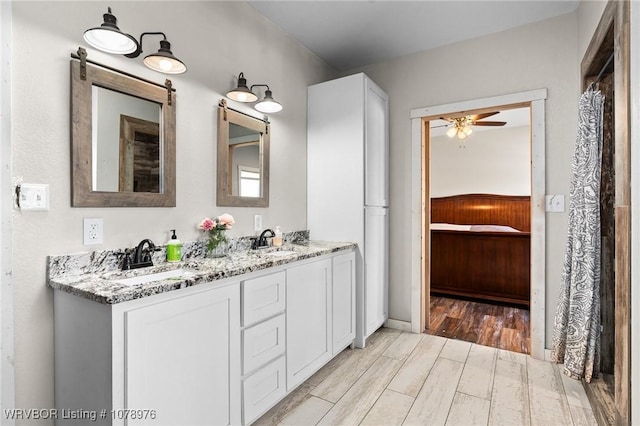 bathroom featuring a sink, wood finished floors, double vanity, and ceiling fan