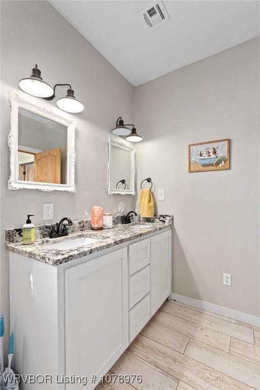 bathroom with double vanity, baseboards, visible vents, and a sink