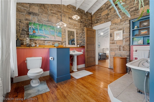 bathroom with toilet, hardwood / wood-style flooring, a tub, and lofted ceiling with beams