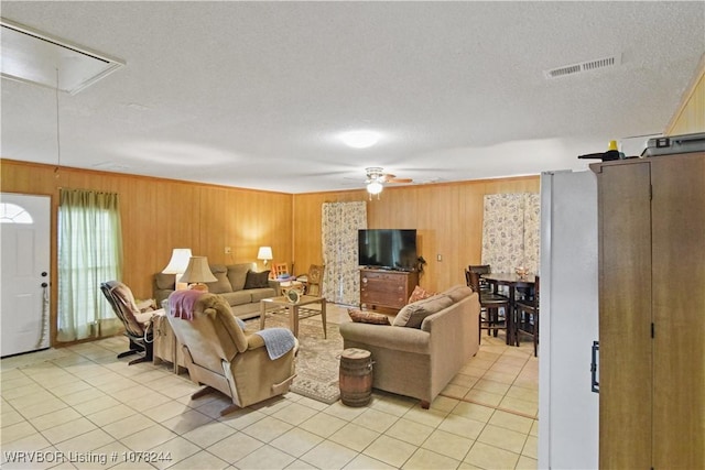 tiled living room featuring ceiling fan, wood walls, and a textured ceiling