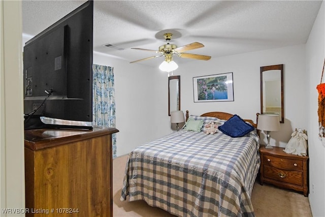 bedroom with ceiling fan, light colored carpet, and a textured ceiling