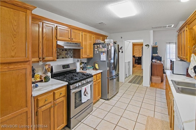 kitchen featuring sink, decorative backsplash, a textured ceiling, appliances with stainless steel finishes, and light tile patterned flooring