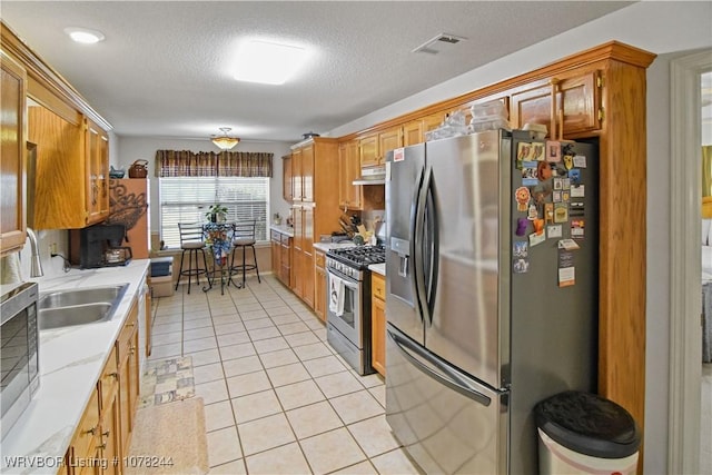 kitchen featuring sink, a textured ceiling, light tile patterned floors, exhaust hood, and appliances with stainless steel finishes