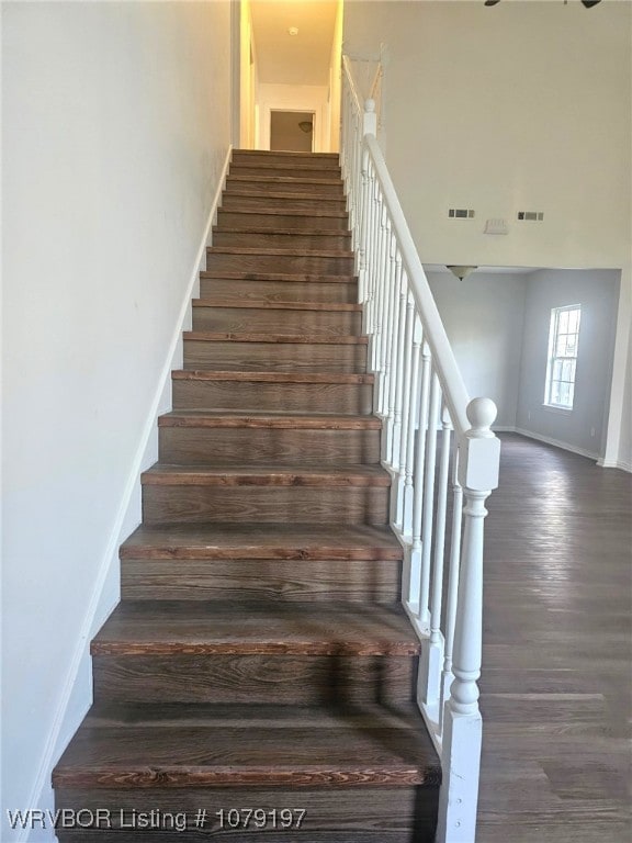 stairs featuring baseboards, visible vents, wood finished floors, and a towering ceiling