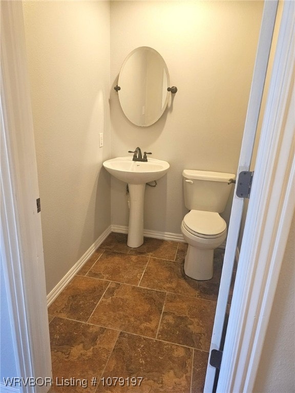 half bathroom with toilet, baseboards, and stone tile flooring