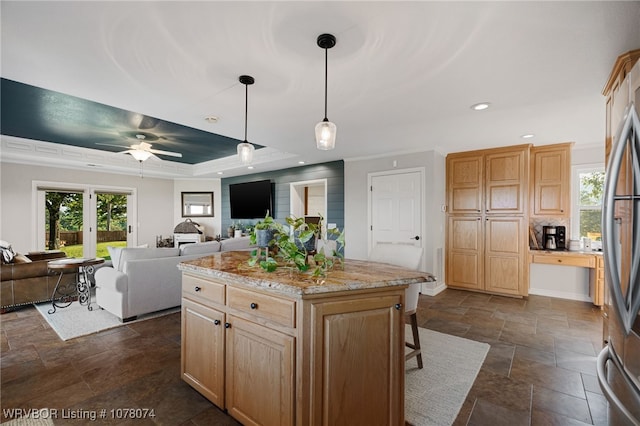 kitchen featuring ceiling fan, a tray ceiling, decorative light fixtures, a kitchen island, and light stone counters