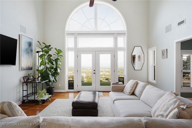 living room featuring ceiling fan, french doors, a towering ceiling, and wood-type flooring