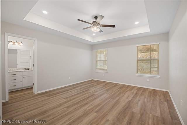 unfurnished bedroom featuring light hardwood / wood-style floors, a raised ceiling, ensuite bath, and ceiling fan