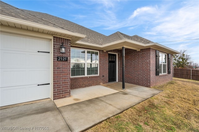 entrance to property with an attached garage, brick siding, fence, roof with shingles, and a lawn