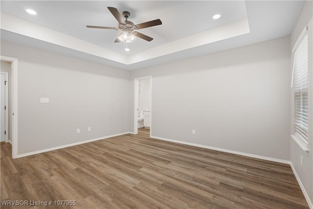 empty room featuring ceiling fan, wood-type flooring, and a tray ceiling