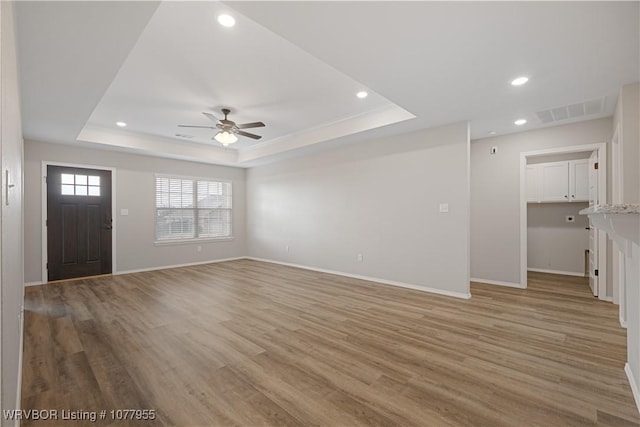 unfurnished living room featuring ceiling fan, a raised ceiling, and light wood-type flooring