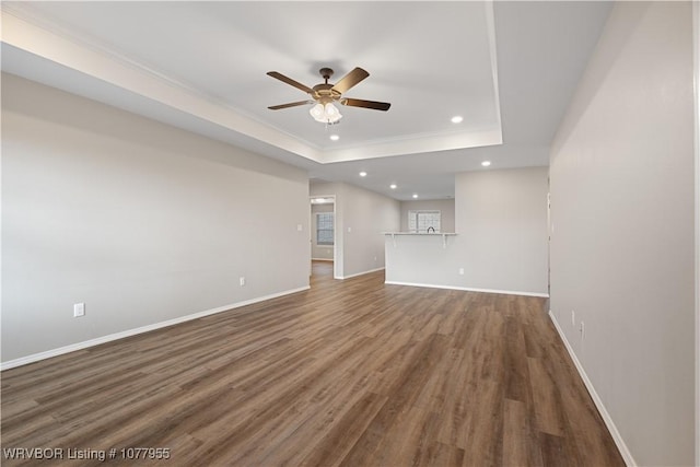 unfurnished living room with ceiling fan, recessed lighting, wood finished floors, baseboards, and a tray ceiling