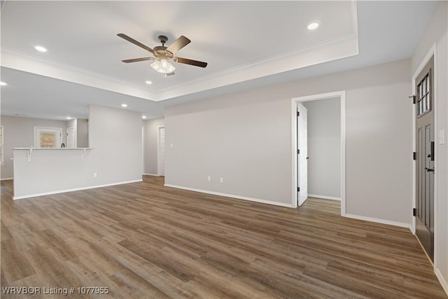 unfurnished living room featuring a tray ceiling, ceiling fan, dark hardwood / wood-style flooring, and crown molding