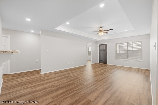 unfurnished living room featuring a tray ceiling, ceiling fan, and light hardwood / wood-style floors