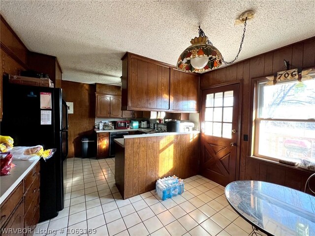 kitchen featuring wood walls, black appliances, light tile patterned floors, a textured ceiling, and kitchen peninsula