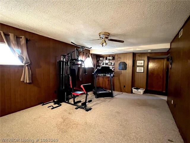 workout area with ceiling fan, light colored carpet, and wooden walls