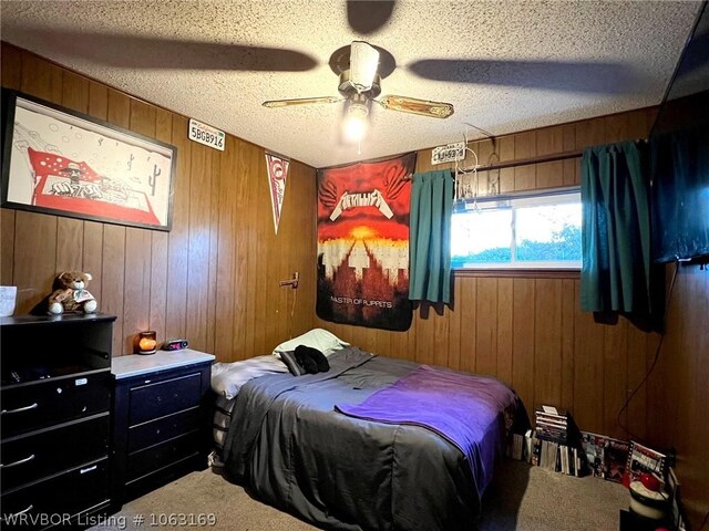 carpeted bedroom featuring ceiling fan, wood walls, and a textured ceiling