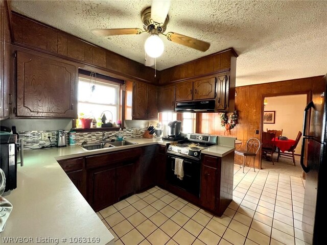 kitchen featuring black refrigerator, gas range oven, ceiling fan, wooden walls, and sink