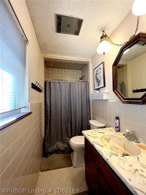 bathroom with walk in shower, tile walls, a textured ceiling, and toilet